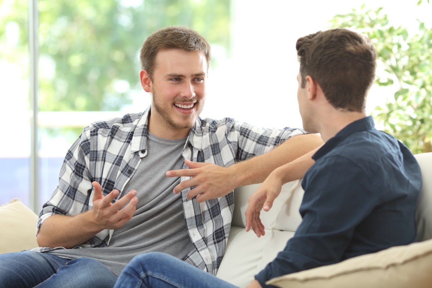 Two men talking on a couch, one gesturing as he speaks